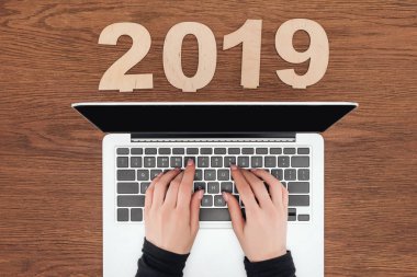 Kırpılan 2019 tarihi ile tahta masada dizüstü bilgisayar kullanan kadın görünümünü kontrplak yapılmış