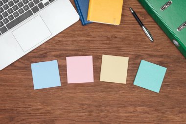 top view of four sticky notes, laptop and office supplies on wooden desk clipart