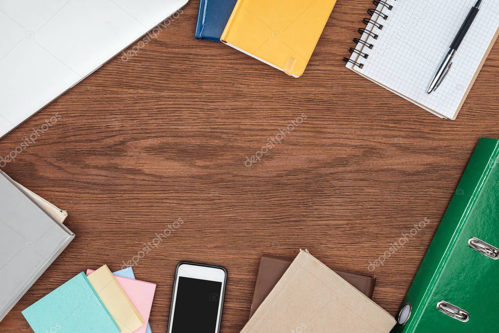 top view of wooden office desk with notebooks and smartphone with blank screen