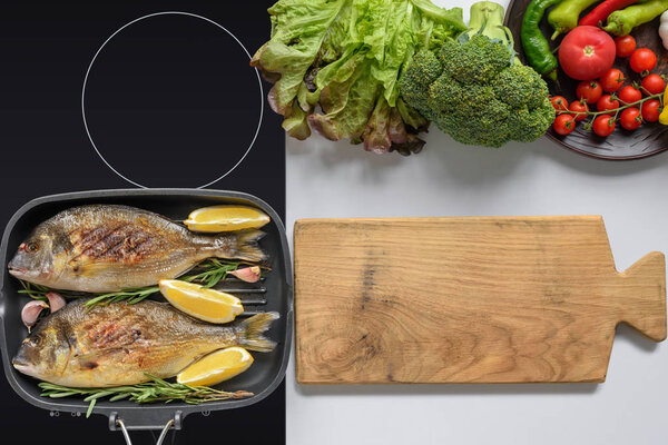 top view of wooden cutting board, fresh vegetables and delicious fried fish on grill