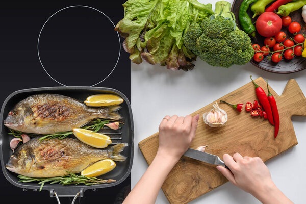 cropped shot of person holding knife and cooking delicious fried fish