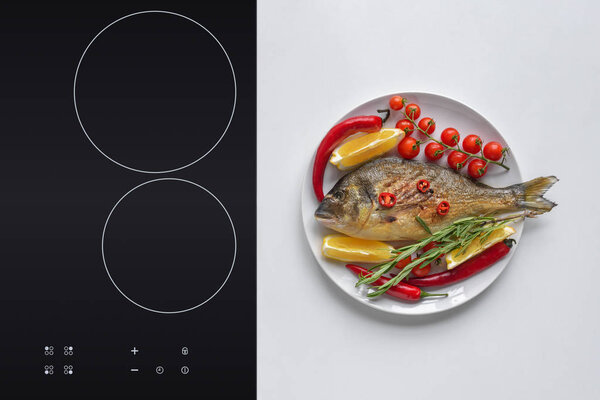 top view of gourmet fried fish with lemon, chili peppers, rosemary and cherry tomatoes on plate