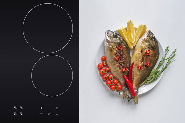 delicious fried fish with cherry tomatoes, rosemary, chili peppers and lemon on plate   