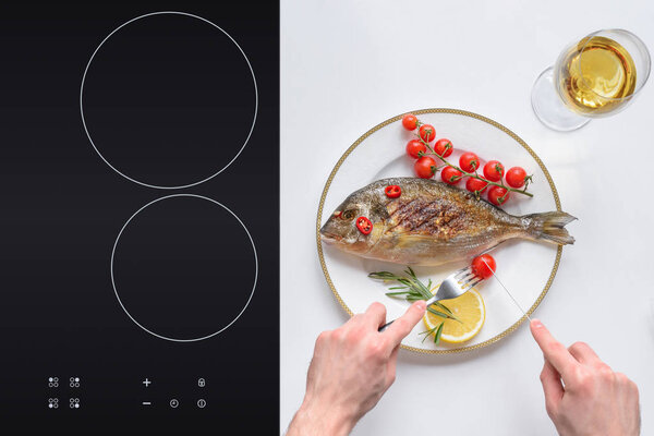 cropped shot of person eating delicious fried dorado fish with cherry tomatoes  