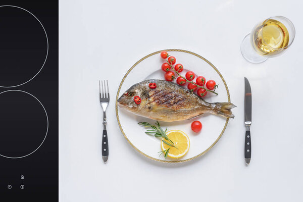 top view of delicious fried fish with cherry tomatoes, lemon and rosemary on plate