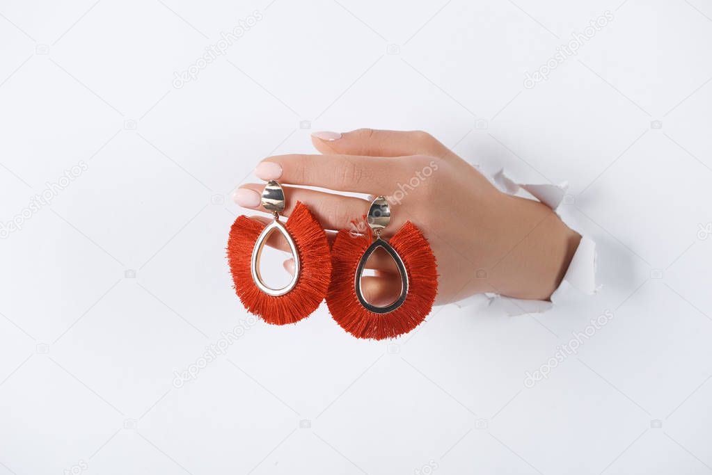 cropped image of woman holding hand with beautiful luxury red earrings through white paper