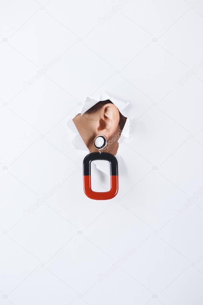 cropped image of woman with beautiful luxury red and black earring standing in hole of white paper