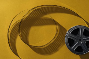 top view of movie reel with twisted cinema tape on yellow background clipart