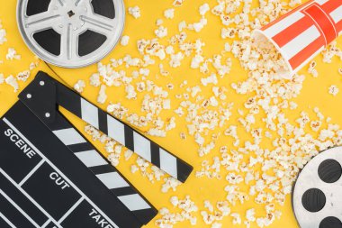 film reels, clapperboard and overturned striped bucket with popcorn isolated on yellow clipart