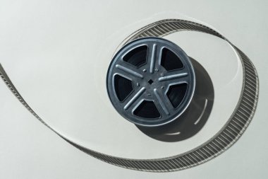 top view of film reel with twisted cinema tape on grey background clipart