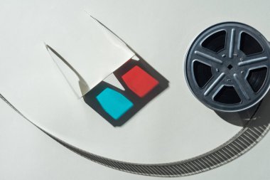 top view of 3d glasses with shadow and film reel with twisted cinema tape on grey background clipart