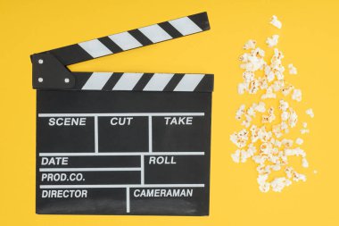 top view of clapperboard and fresh crunchy popcorn isolated on yellow clipart