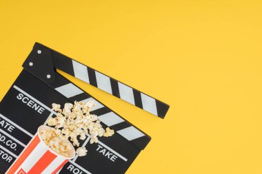 cinema clapperboard and overturned bucket with popcorn isolated on yellow clipart