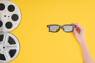 Film makaraları ve sarı izole Stereoskopik 3d gözlük tutan el