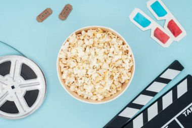 top view of clapperboard, film reel, 3d glasses, cinema tickets and popcorn bucket isolated on blue clipart