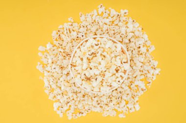 top view of carton bucket and scattered popcorn isolated on yellow clipart