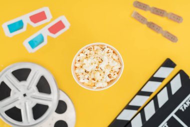 top view of clapperboard, film reels, 3d glasses, cinema tickets and popcorn bucket isolated on yellow clipart