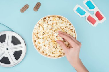 film makarası, 3d gözlük, sinema biletleri ve mavi izole kova patlamış mısır alarak el üstten görünüm