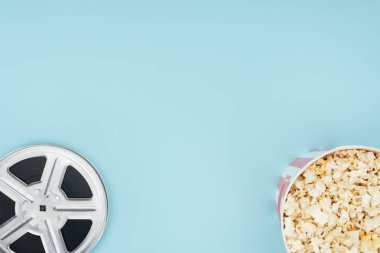top view of film reel and popcorn in bucket isolated on blue clipart