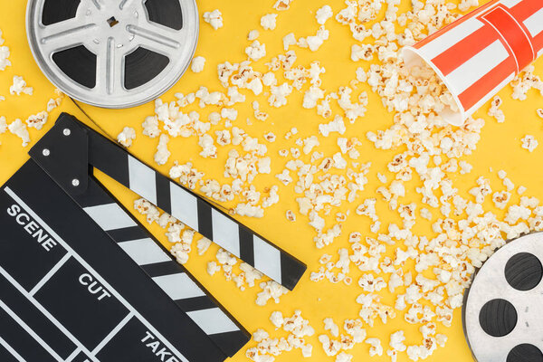 film reels, clapperboard and overturned striped bucket with popcorn isolated on yellow