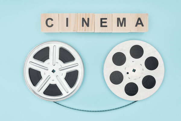wooden cubes with "cinema" lettering and film reels with cinema tape between them isolated on blue