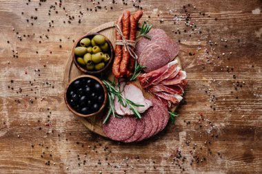 yuvarlak kesme tahtası lezzetli salam, jambon ve zeytin iki kase ile üstten görünüm dağınık baharat ahşap tablo