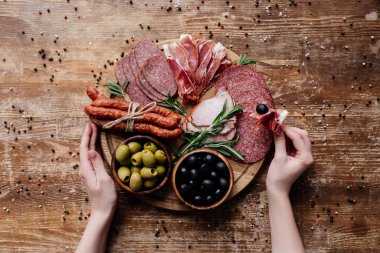 ahşap masa dağınık karabiber ile prosciutto zeytin, salam ve jambon ile yuvarlak kesme tahtasından alarak kadının kırpılmış görünümü