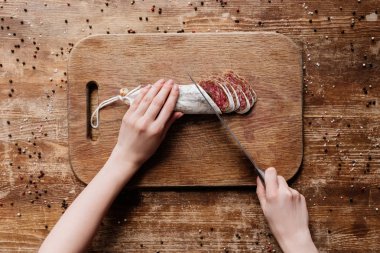Ahşap tahta üzerinde çelik bıçak ile kadın kesme lezzetli salam görünümünü kırpılmış