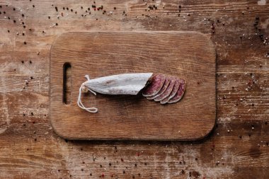dikdörtgen kesme tahtası ile lezzetli dilimlenmiş salam üstten görünüm dağınık baharat ahşap tablo
