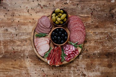 üst kesme tahtası zeytinli yuvarlak ve dilimlenmiş salam, jambon ve jambon dağınık baharat ahşap tablo