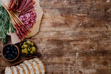 Kesme tahtaları lezzetli jambon, salam, ekmek, zeytin ve otlar ile üstten görünüm dağınık baharat ahşap tablo