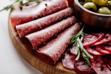 close up view of delicious sliced salami with rosemary and peppercorns on wooden cutting board clipart