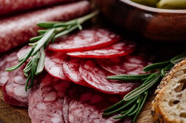 close up view of delicious sliced salami with rosemary and bread on wooden cutting board