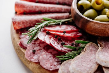 close up view of delicious sliced salami with spices and olives in bowl on wooden cutting board clipart