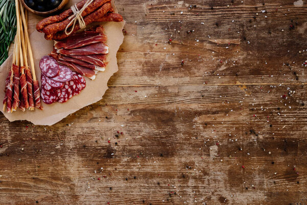 top view of cutting board with sliced prosciutto, salami and smoked sausages on wooden vintage table  with scattered spices
