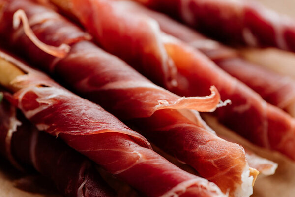 close up view of delicious sliced prosciutto wrapped around breadsticks
