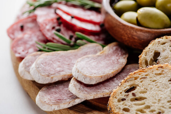 close up view of delicious sliced salami, bread and olives in bowl on wooden cutting board