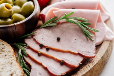 close up view of olives in bowl and delicious sliced ham with spices and herbs on wooden cutting board clipart
