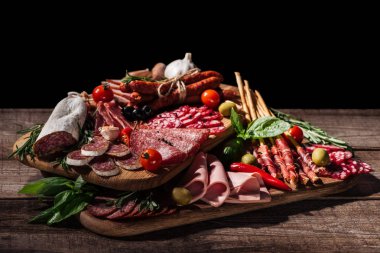 cutting boards with delicious salami, smoked sausages, ham, vegetables and herbs on wooden rustic table clipart