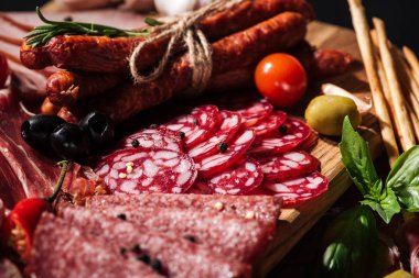 close up view of delicious smoked sausages and sliced salami with vegetables on wooden cutting board clipart