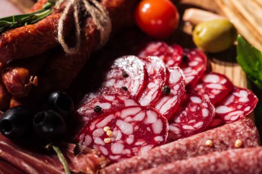 close up view of delicious sliced salami with vegetables and spices on wooden cutting board clipart