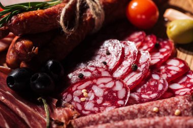 close up view of delicious sliced salami with vegetables and spices on wooden cutting board clipart