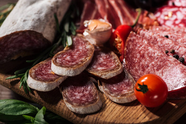 close up view of sliced salami with vegetables on wooden cutting board