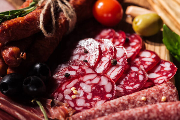 close up view of delicious sliced salami with vegetables and spices on wooden cutting board