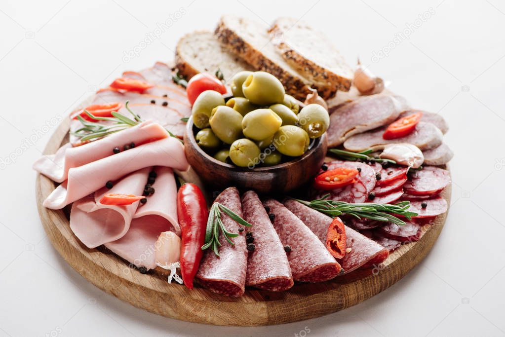 round cutting board with olives in bowls, delicious salami, ham, sausages bread and vegetables on brown wrapping paper