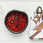 Top view of traditional beetroot soup with cutlery and glass of vodka on white wooden background