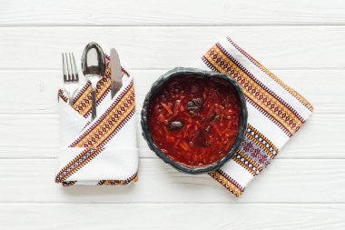 Beyaz ahşap zemin üzerine işlemeli havlu ve çatal bıçak takımı ile geleneksel Pancar çorbası üstten görünüm