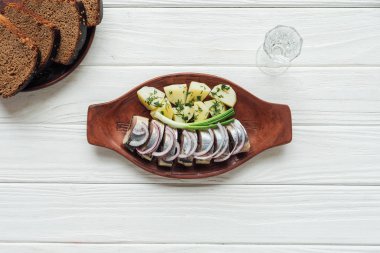 Ringa balığı, patates ve soğan toprak plaka ile kadeh votka ve çavdar ekmeği Beyaz ahşap zemin üzerinde Marine