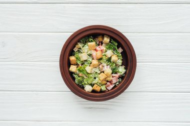 top view of tasty caesar salad with croutons in bowl on white wooden background clipart
