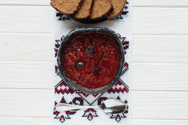 bowl of traditional beetroot soup with embroidered towel and rye bread on white wooden background clipart